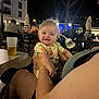 baby, child, person, adult, night, outdoor, dining, restaurant, table, chair, drink, beverage, stroller, clothing, smile, happy, light, people, arm, face