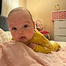 Khloe is registered to the contest to win money with this photo: baby, infant, yellow_onesie, blanket, bedroom, bed, furniture, face, eyes, skin, head, person, indoors, soft_texture, curious, expression, child, pink, cozy, sleepwear