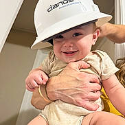 Waylon joined the competition — help win amazing prizes! adult, apparel, baby, child, closeup, construction_helmet, cute, drool, face, hands, happy, headwear, helmet, holding, indoor, infant, onesie, person, skin, smiling