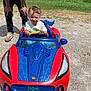 Olliemore joined the competition — help win amazing prizes! toddler, child, toy_car, spiderman, red, blue, outdoor, grass, gravel, adult, person, smiling, steering_wheel, playing, sunny, casual_clothing, watch, shoes, fun, happy