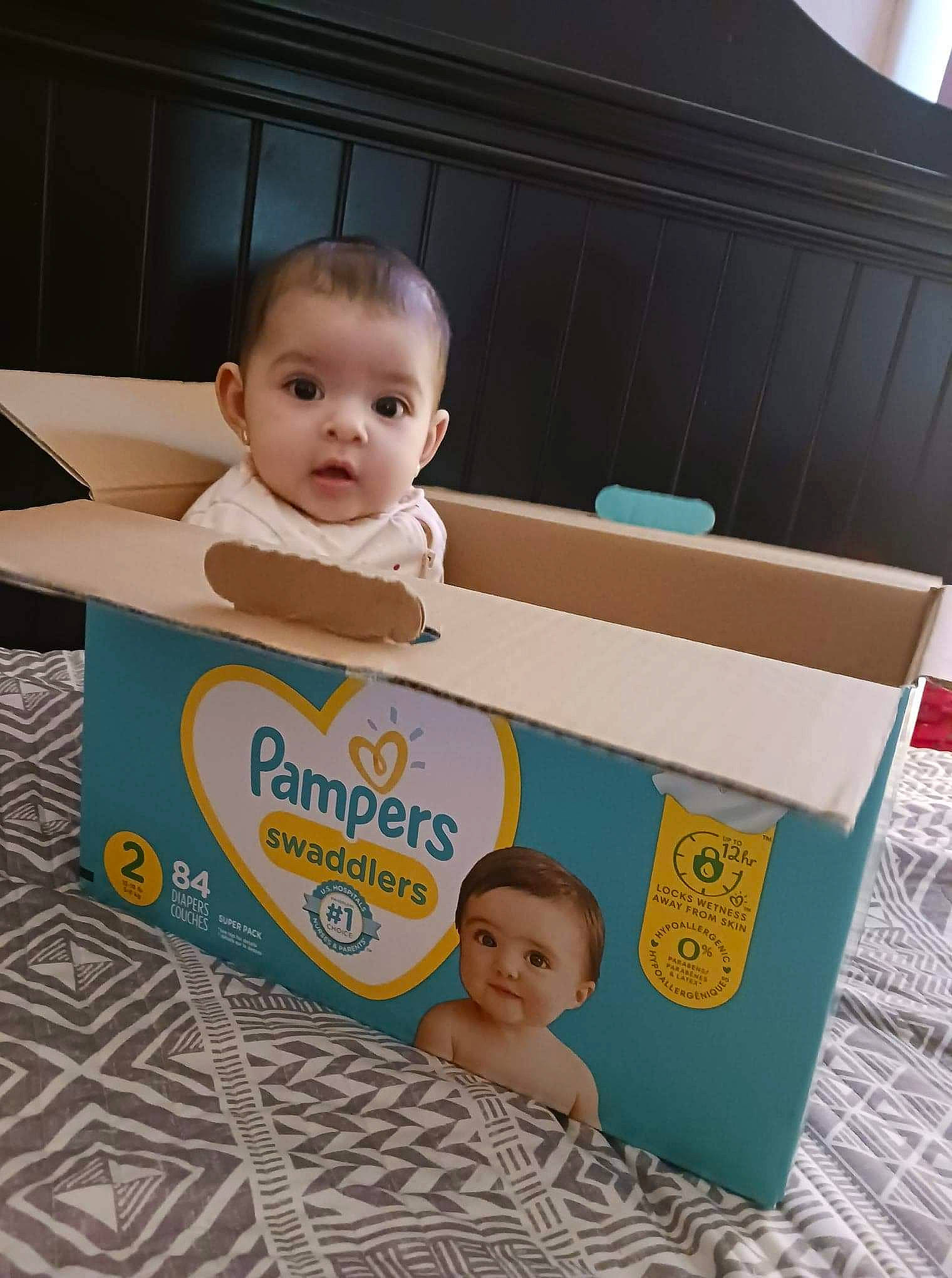 Itzel is registered to the contest to win money with this photo: baby, baby_products, baby_safety, baby_toddler_clothing, box, carton, child, face, facial_expression, hairstyle, happy, packaging_and_labeling, packing_materials, person, play, product, rectangle, room, shipping_box, smile