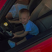 Daïron participe au concours pour gagner de l'argent avec cette photo : toddler, child, car, steering_wheel, red_car, white_dress, seat, seatbelt, smile, playing, interior, vehicle, happy, person, footwear, sneakers, daylight, window, hand, fun