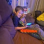 Cookie is registered to the contest to win money with this photo: boy, dog, couch, handheld_device, smile, indoor, lamp, holiday_card, brown_couch, curtain, casual_clothing, child, pet, toy, relaxation, home, happy, technology, furniture, cozy