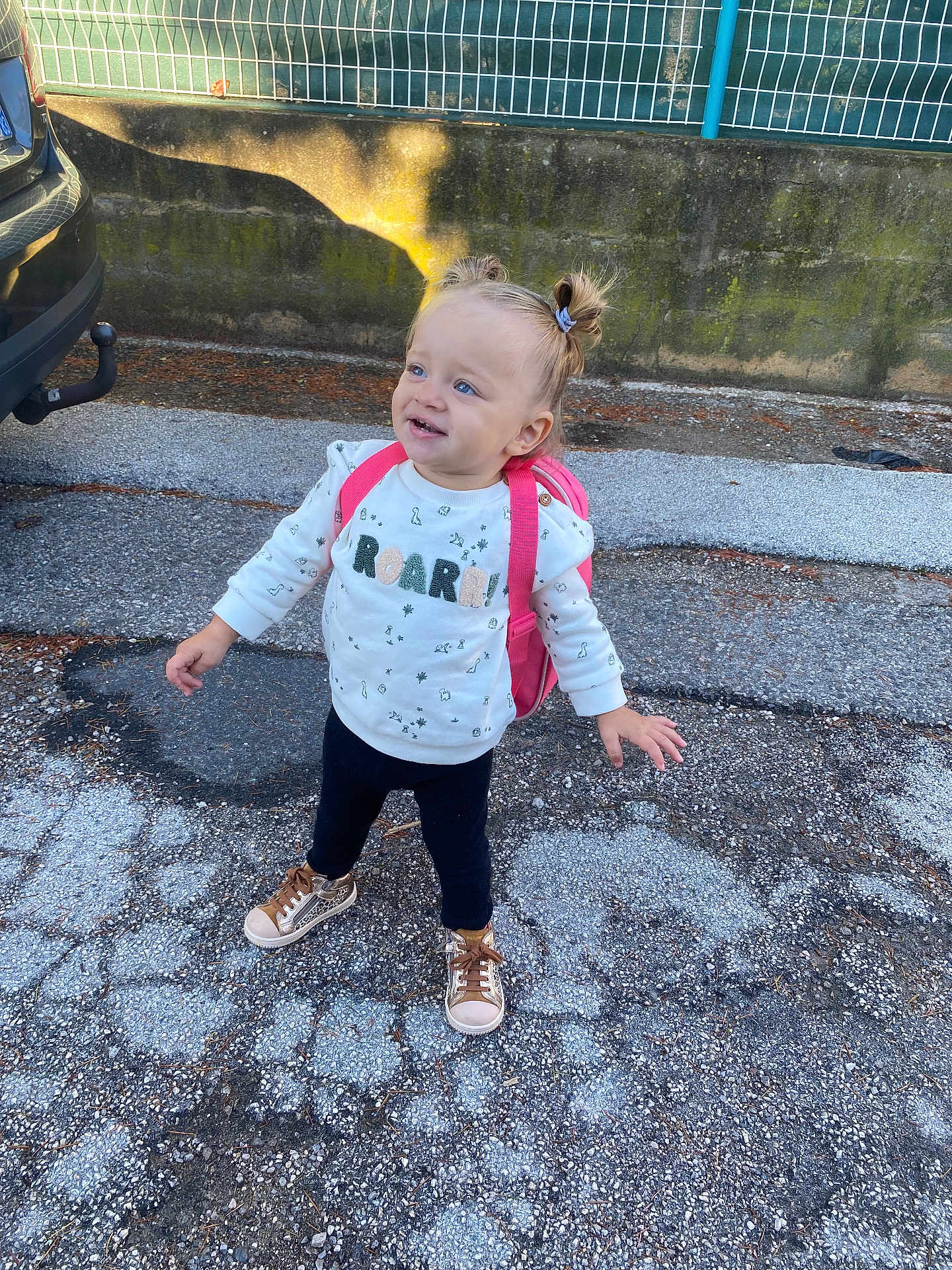 Camila a rejoint le concours — aidez-le/la à gagner de superbes lots ! toddler, child, outdoor, pavement, backpack, sweater, pigtails, shoes, curly_hair, sunlight, shadow, fence, concrete, wall, playful, standing, happy, casual_clothing, young_child, smiling