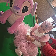 Yara a rejoint le concours — aidez-le/la à gagner de superbes lots ! adult, background, casual_clothing, child, cute, furniture, green_surface, hand, headband, home, indoor, kitchen, person, pink_dress, plush_toy, pool_table, seated, support, toddler, toy