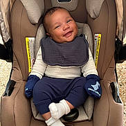 Julius is registered to the contest to win money with this photo: baby, car_seat, smile, mittens, white_socks, navy_pants, bib, infant, seat, child, cute, happy, portrait, cozy, indoor, clothing, person, baby_garment, newborn, comfort