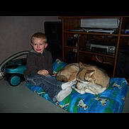 Nina a rejoint le concours — aidez-le/la à gagner de superbes lots ! boy, child, dog, blanket, indoor, floor, vacuum_cleaner, sitting, curled_up, furniture, shelf, electronics, casual_clothing, blue, brown, home, pet, cozy, relaxed, carpet