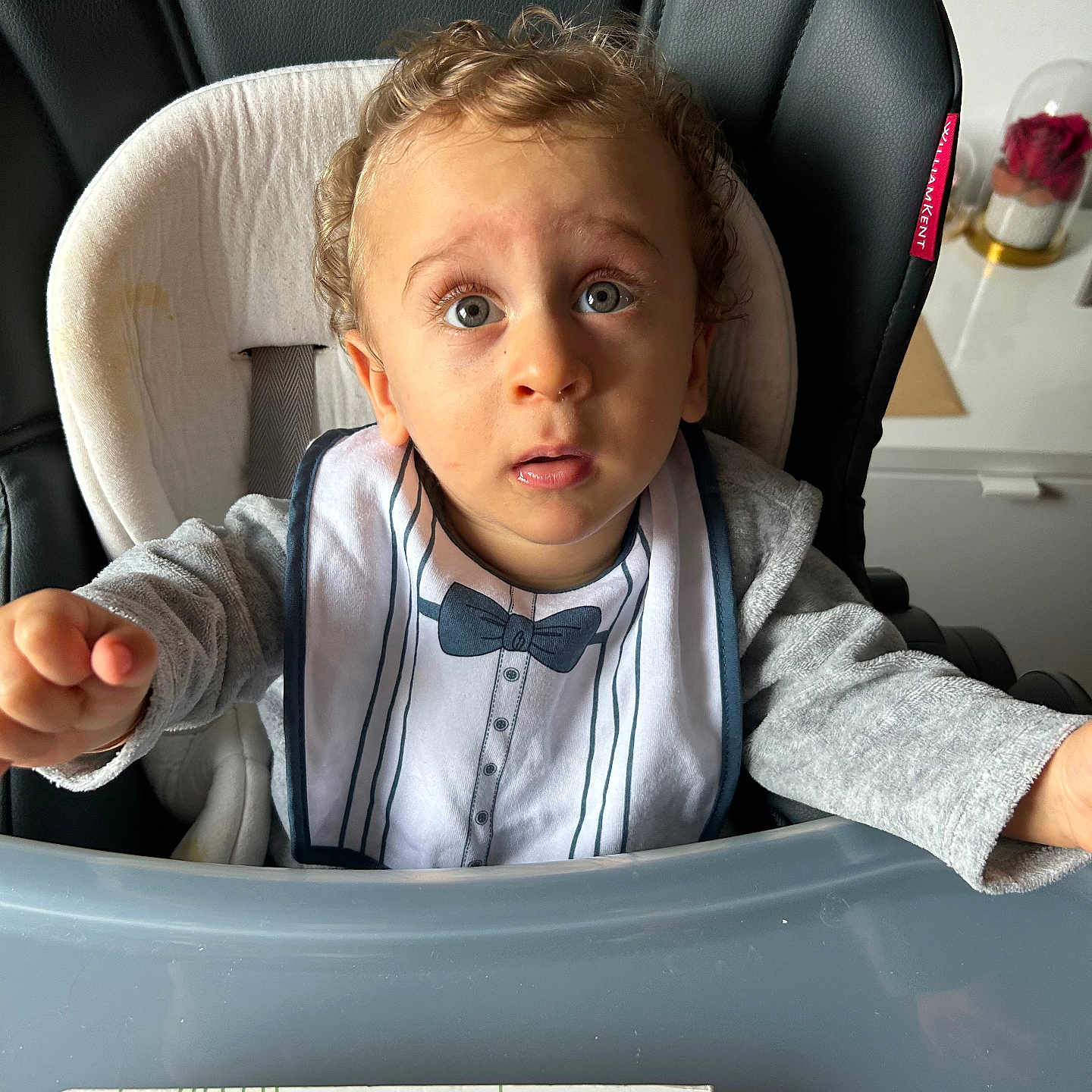 Florentin participe au concours pour gagner de l'argent avec cette photo : baby, bib, blue, child, clothing, curious, curly_hair, expression, face, furniture, gray, high_chair, indoor, person, pink, seat, table, toddler, toy, tray