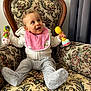 baby, child, armchair, rattle, pink_bib, curly_hair, smiling, happy, indoor, clothing, sweater, pants, footed_pants, furniture, floral_pattern, vintage, person, portrait, cute, seated