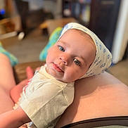 Millie is registered to the contest to win money with this photo: baby, child, infant, face, headwear, blue_eyes, white_shirt, person, indoor, blurred_background, home, lap, skin, cute, looking, soft_light, casual, relaxed, portrait, human