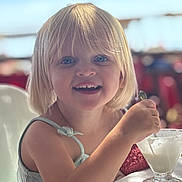 Julia participe au concours pour gagner de l'argent avec cette photo : child, toddler, blonde_hair, blue_eyes, smile, spoon, dessert, glass_cup, ice_cream, high_chair, dining_table, close_up, portrait, candid, happy, bangs, sleeveless_top, soft_lighting, background_bokeh, family_restaurant