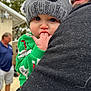 Charlie joined the competition — help win amazing prizes! baby, child, person, hat, knit_hat, finger_sucking, beard, man, green_clothing, black_clothing, outdoor, blurred_background, house, tree, adult, close_up, cute, winter_clothing, holding, portrait