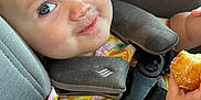 Charlie is registered to the contest to win money with this photo: toddler, child, car_seat, seatbelt, food, pastry, smile, face, blue_eyes, clothing, colorful, cute, baby, arm, indoor, seat, happy, person, closeup, mischievous