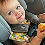 toddler, child, car_seat, seatbelt, food, pastry, smile, face, blue_eyes, clothing, colorful, cute, baby, arm, indoor, seat, happy, person, closeup, mischievous