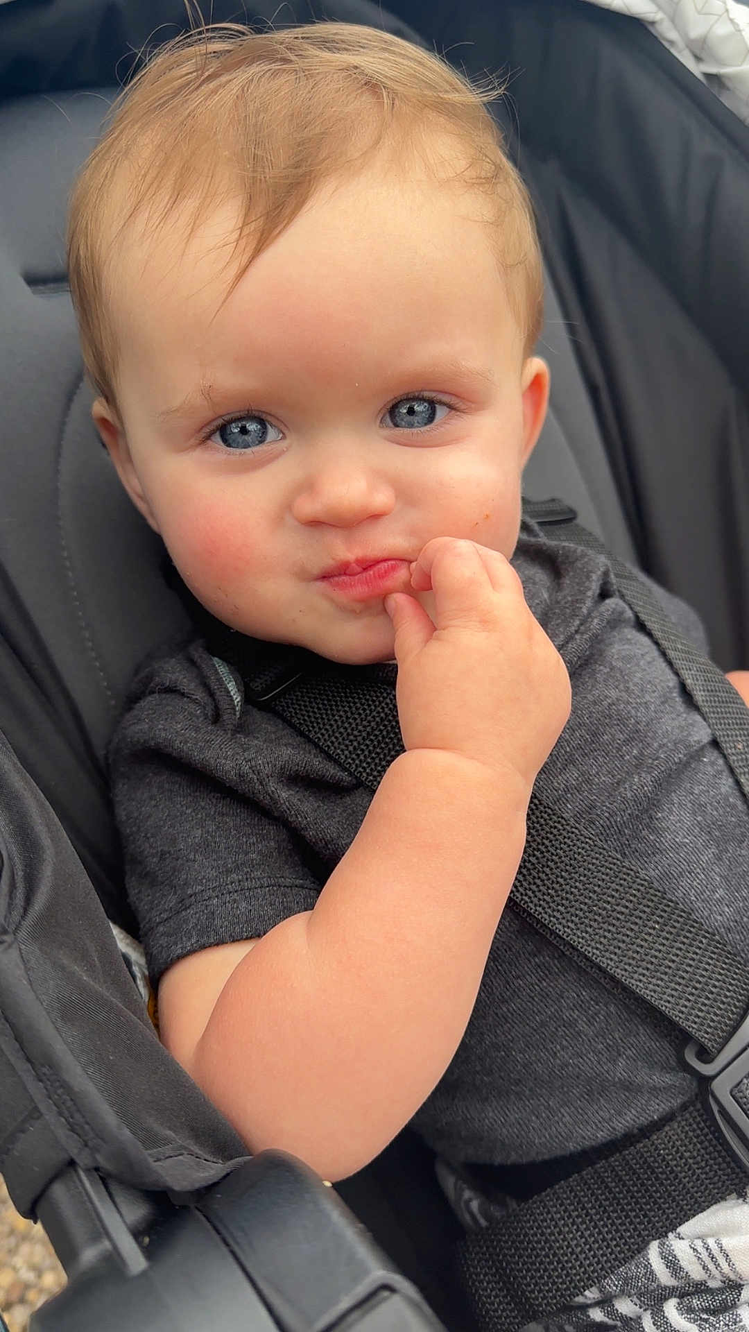 Charlie is registered to the contest to win money with this photo: toddler, child, baby, blue_eyes, hand, stroller, seatbelt, clothing, black_shirt, cute, face, portrait, outdoor, curious, expression, skin, hair, person, seat, closeup