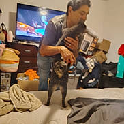 Chase joined the competition — help win amazing prizes! bed, blanket, blur, box, casual_clothing, cat, clutter, drawer, furniture, hair, hand, holding, indoor, man, pet, room, shadow, television, television_screen, wall