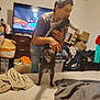 bed, blanket, blur, box, casual_clothing, cat, clutter, drawer, furniture, hair, hand, holding, indoor, man, pet, room, shadow, television, television_screen, wall