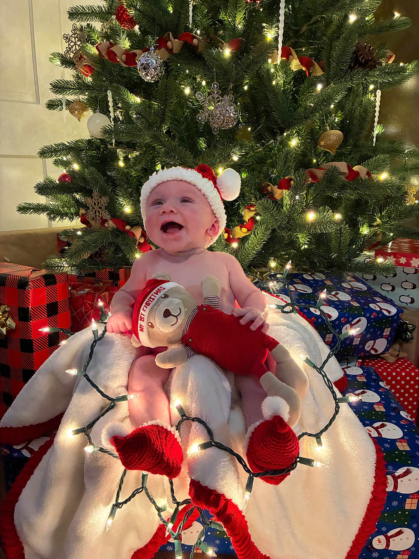 David joined the competition — help win amazing prizes! baby, christmas_tree, christmas_lights, teddy_bear, santa_hat, blanket, presents, holiday, festive, smiling, indoor, decorations, red, green, white, child, happy, celebration, toy, cozy