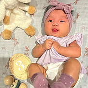 Liara is registered to the contest to win money with this photo: baby, infant, headband, socks, blanket, stuffed_animal, toy, rattle, milestone_card, lying_down, tongue_out, cute, pink, purple, wooden_toy, bunny_pattern, child, soft_toy, playful, clothing