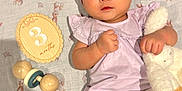Liara is registered to the contest to win money with this photo: baby, infant, headband, socks, stuffed_animal, toy, wooden_rattle, milestone_plaque, blanket, bunny_pattern, purple_clothing, cute, lying_down, indoors, child, person, soft_toys, baby_girl, adorable, milestone