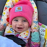 Dafne is registered to the contest to win money with this photo: baby, child, smiling, pink_beanie, floral_pattern, car_seat, cushion, happy, cute, infant, clothing, portrait, face, headwear, seatbelt, colorful, outdoor, warm_clothing, closeup, person