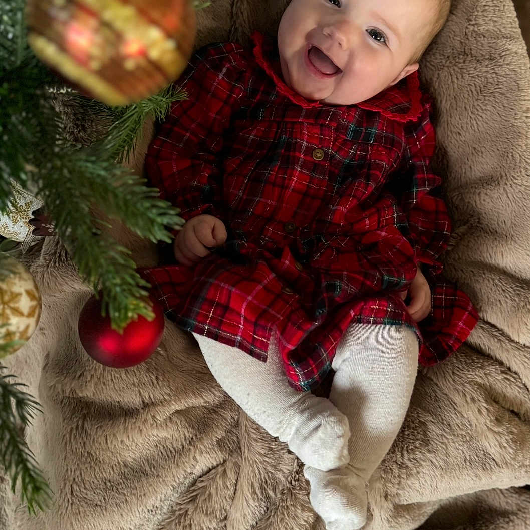 Elsie joined the competition — help win amazing prizes! baby, blanket, celebration, child, christmas_tree, cozy, cute, face, festive, happy, holiday, indoors, infant, ornaments, plaid, red_dress, seasonal, smiling, soft_texture, white_tights