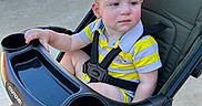 Grady is registered to the contest to win money with this photo: baby, barefoot, candid, child, concrete, cupholder, expression, fabric_seat, grasping_hand, outdoor, picnic_table, portrait, seatbelt, striped_shirt, stroller, stroller_wheel, sunny, toddler, tray, yellow_shirt