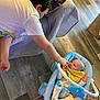 Grady joined the competition — help win amazing prizes! baby, baby_seat, carpet, child, couch, cozy, curious, floor, frog_slippers, hand_touching, indoor, infant, person, pillow, playful, sibling_interaction, toy_bar, white_shirt, wood_floor, yellow_bib
