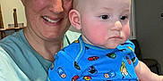 Grady is registered to the contest to win money with this photo: adult, baby, blue, bracelet, casual, chair, child, family, holding, home, indoor, person, picture_frame, portrait, serious, shirt, shorts, smiling, superhero, wall_clock