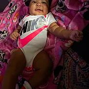 Amariaya is registered to the contest to win money with this photo: baby, infant, smiling, onesie, nike, blanket, pink, minnie_mouse, pattern, clothing, child, cute, happy, lying_down, indoors, face, person, footwear, socks, portrait