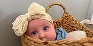 Bella is registered to the contest to win money with this photo: baby, infant, basket, wicker, headband, bow, blue_clothing, big_eyes, peeking, portrait, indoor, wall, hardwood_floor, cozy, woven_texture, cute, head, sitting, blanket, home_interior