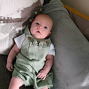 Leonard is registered to the contest to win money with this photo: baby, infant, couch, pillow, green_romper, white_socks, indoor, portrait, child, cute, relaxing, soft_texture, cozy, seated, looking_up, small_hands, wide_eyes, curious, comfortable, home