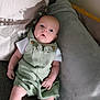 baby, infant, couch, pillow, green_romper, white_socks, indoor, portrait, child, cute, relaxing, soft_texture, cozy, seated, looking_up, small_hands, wide_eyes, curious, comfortable, home