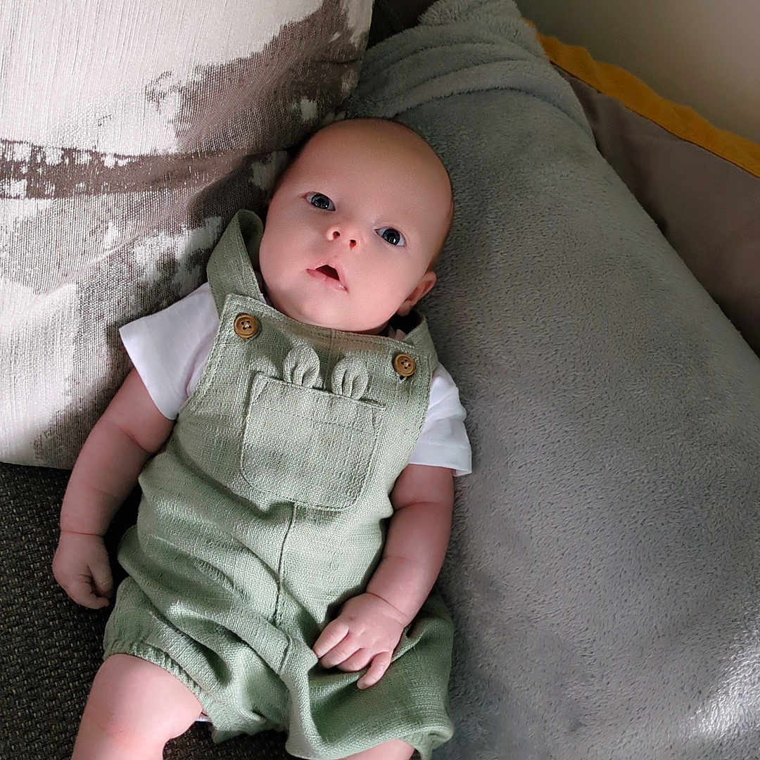 Leonard is registered to the contest to win money with this photo: baby, child, comfortable, couch, cozy, curious, cute, green_romper, home, indoor, infant, looking_up, pillow, portrait, relaxing, seated, small_hands, soft_texture, white_socks, wide_eyes