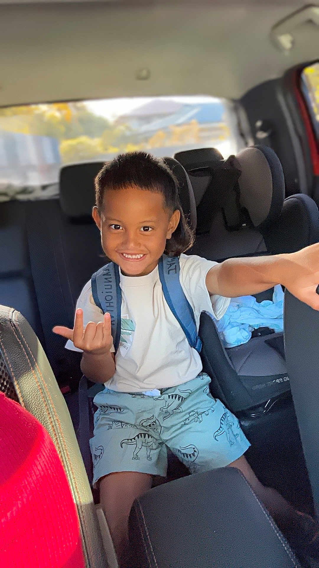 Tepoeanuiohiva a rejoint le concours — aidez-le/la à gagner de superbes lots ! child, boy, smile, backseat, car_interior, car_seat, backpack, dinosaur_shorts, white_tshirt, shorts, short_hair, hand_gesture, pointing, happy, portrait, sunlit, window, road_trip, family, upholstery