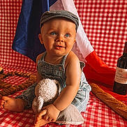 Liam participe au concours pour gagner de l'argent avec cette photo : baby, denim_overalls, cap, stuffed_animal, red_and_white_checkered, french_flag, wine_bottle, wine_glass, baguette, wine_corks, picnic, child, smiling, sitting, indoor, cute, portrait, cloth, food, drink