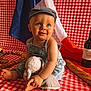baby, denim_overalls, cap, stuffed_animal, red_and_white_checkered, french_flag, wine_bottle, wine_glass, baguette, wine_corks, picnic, child, smiling, sitting, indoor, cute, portrait, cloth, food, drink