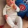baby, child, infant, pajamas, bib, snack, waffle, cushion, plush_pillow, logo, indoor, sitting, hand, face, blue_eyes, clothing, bed, comfort, relaxed, cute