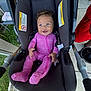 baby, car_seat, pink_onesie, smiling, curly_hair, blue_eyes, infant, outdoor, grass, sidewalk, person, happy, clothing, footed_pajamas, child, seatbelt, fabric, hand, portrait, cute