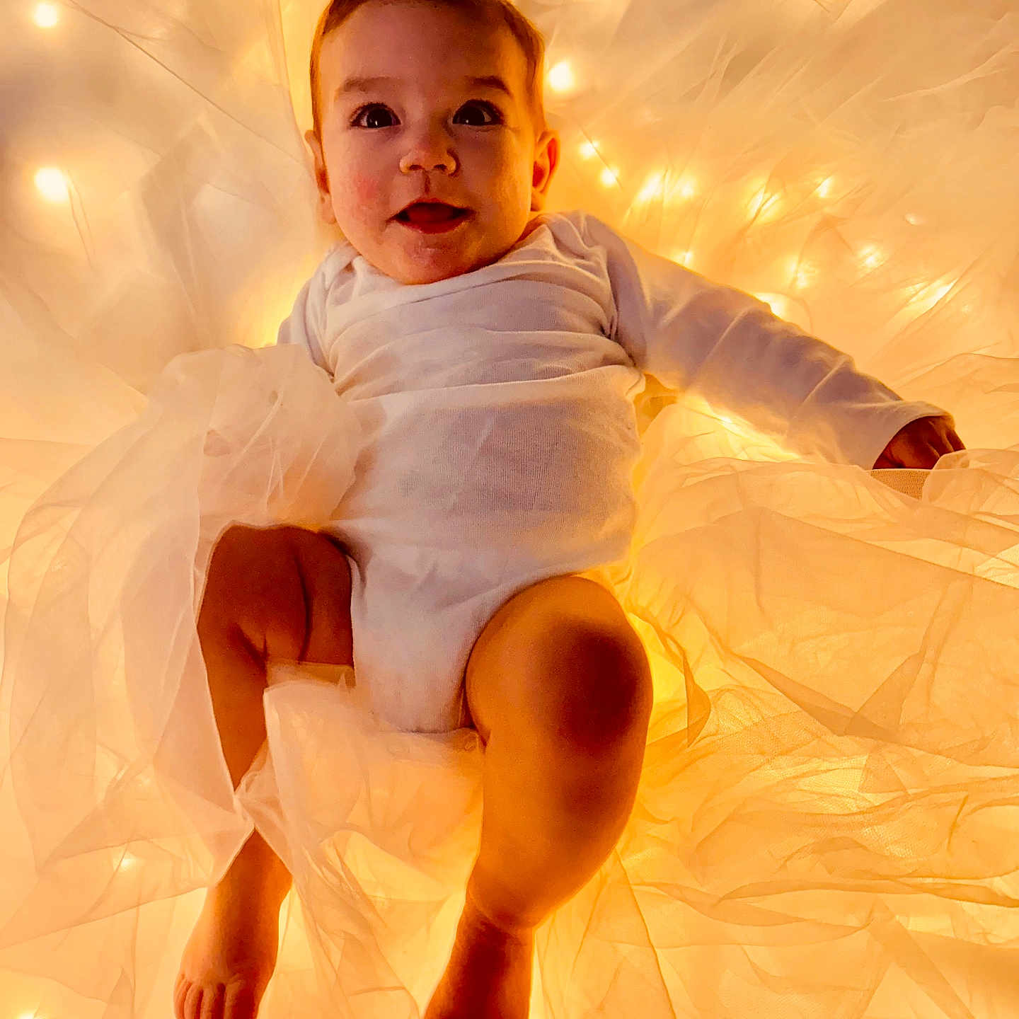 Rosalie is registered to the contest to win money with this photo: baby, bodypart, clothing, dress, face, finger, formalwear, furniture, hand, happy, hardwood, head, light, lighting, person, photography, portrait, sitting, smile, wood