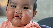 Catalina is registered to the contest to win money with this photo: baby, child, face, cheeks, pigtails, hair, mouth, crumbs, shirt, butterfly, orange, peach, cute, expression, blurred_background, infant, portrait, sitting, high_chair, outdoor