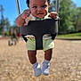 toddler, child, swing, playground, outdoor, happy, smiling, curly_hair, white_shoes, shorts, sunny, daylight, blurred_background, fists, baby, seat, park, fun, cute, person