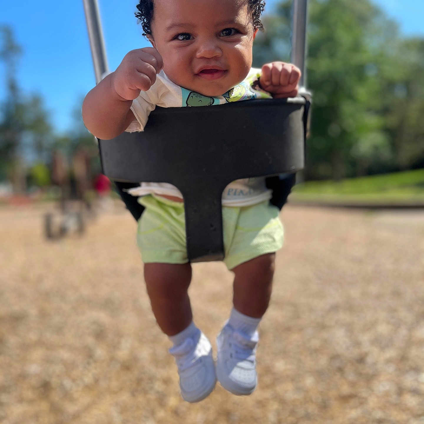 Jaiteek is registered to the contest to win money with this photo: baby, blurred_background, child, curly_hair, cute, daylight, fists, fun, happy, outdoor, park, person, playground, seat, shorts, smiling, sunny, swing, toddler, white_shoes