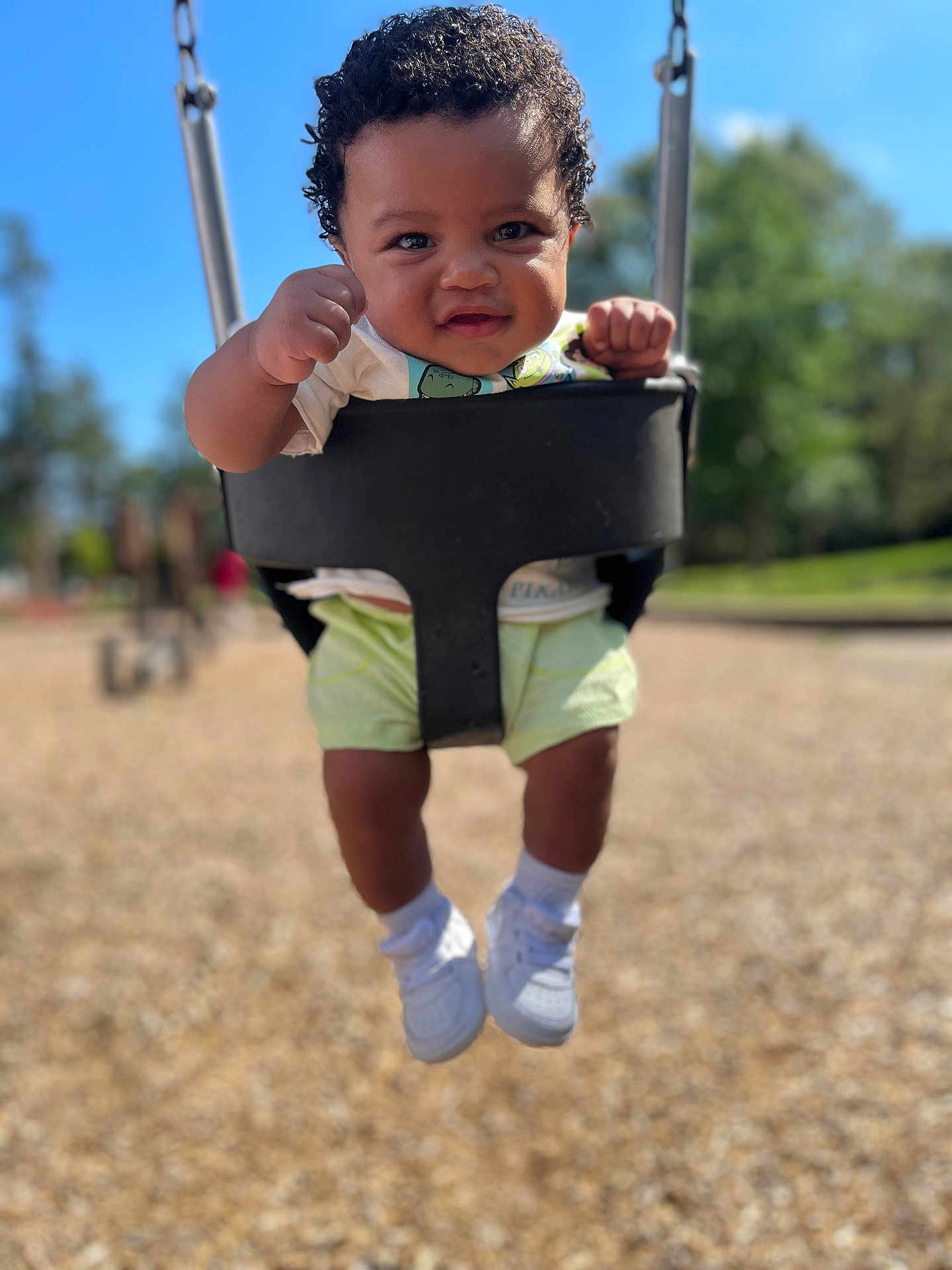 Jaiteek is registered to the contest to win money with this photo: toddler, child, swing, playground, outdoor, happy, smiling, curly_hair, white_shoes, shorts, sunny, daylight, blurred_background, fists, baby, seat, park, fun, cute, person