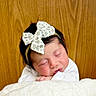 Charlotte is registered to the contest to win money with this photo: newborn, baby, sleeping, infant, portrait, face, floral_bow, headband, blanket, white_blanket, white_clothing, hands, closed_eyes, peaceful, cozy, indoor, wood_background, close_up, resting, photography