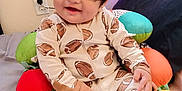 Gino is registered to the contest to win money with this photo: baby, child, smiling, pajamas, football_pattern, cushion, colorful, indoor, happy, face, hair, sitting, plush, bed, blanket, person, cute, cozy, infant, home