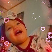 Gena is registered to the contest to win money with this photo: baby, child, headband, bow, floral_clothing, smiling, happy, indoor, person, sparkles, hearts, christmas_tree, holiday, portrait, face, cute, joy, celebration, infant, warm_lighting