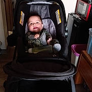 James is registered to the contest to win money with this photo: child, baby, stroller, indoor, smile, pajamas, face, furniture, door, bottle, wooden_floor, microwave, cabinet, curiosity, happy, person, infant, room, footwear, household