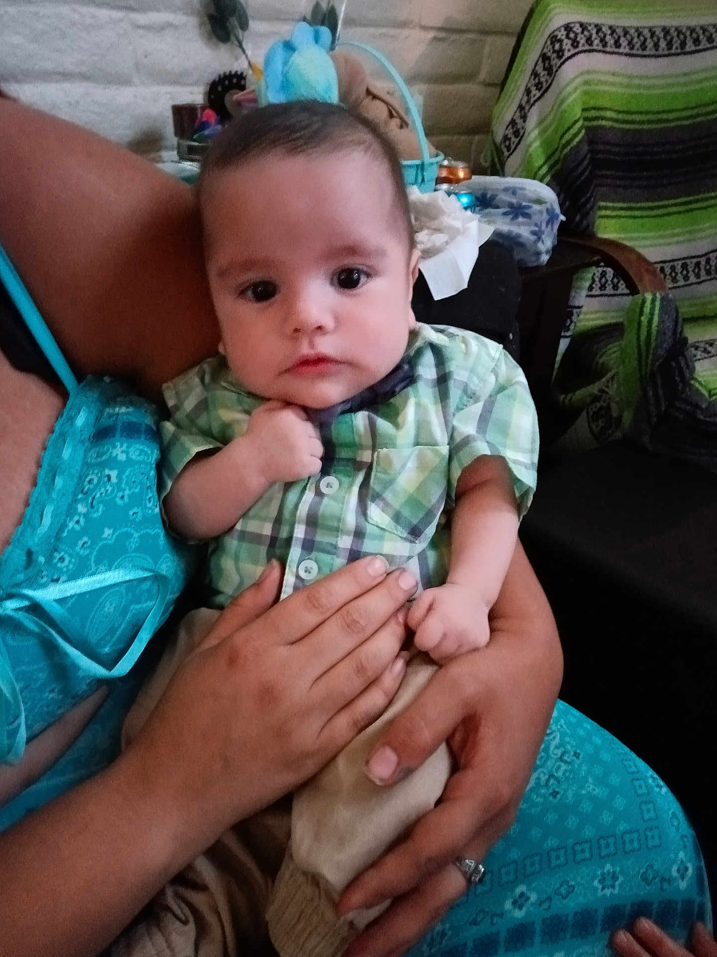 James is registered to the contest to win money with this photo: baby, child, person, plaid_shirt, hands, arm, clothing, indoor, furniture, blanket, seat, portrait, cute, infant, skin, face, young, holding, sitting, casual