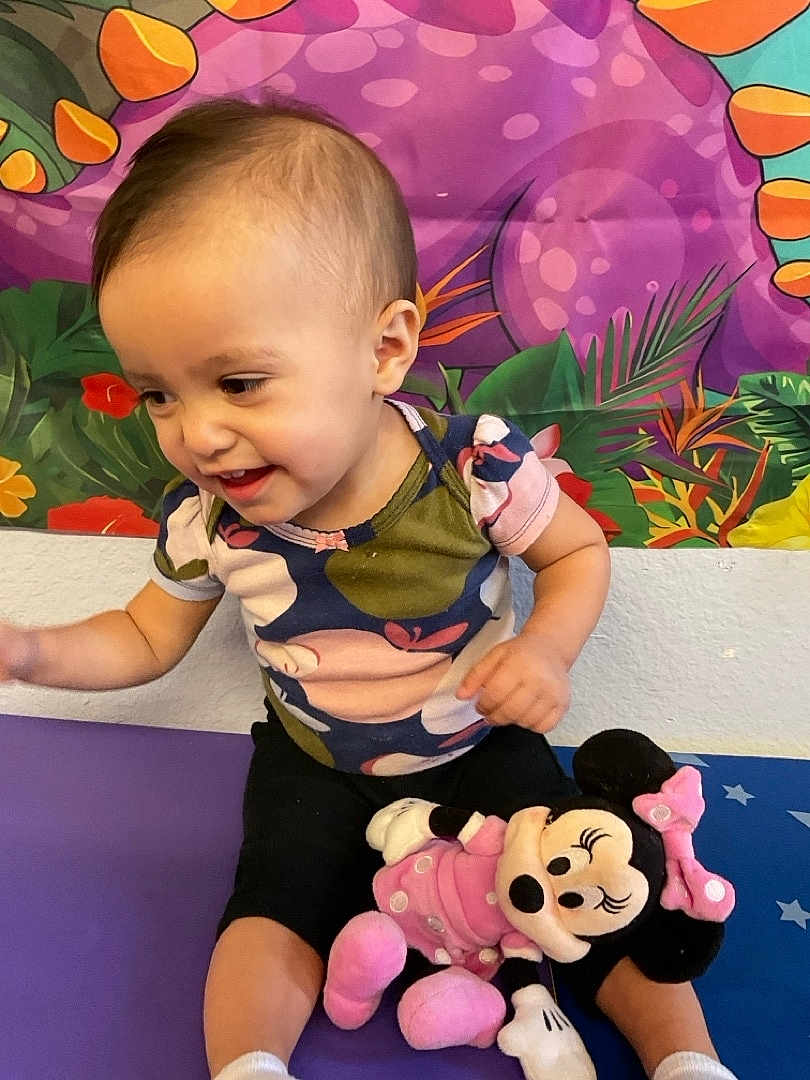Gena is registered to the contest to win money with this photo: baby, toddler, child, smiling, sitting, plush_toy, minnie_mouse, colorful_background, wall_art, onesie, shorts, indoor, playtime, cute, happy, portrait, hair, cheek, arm, toy